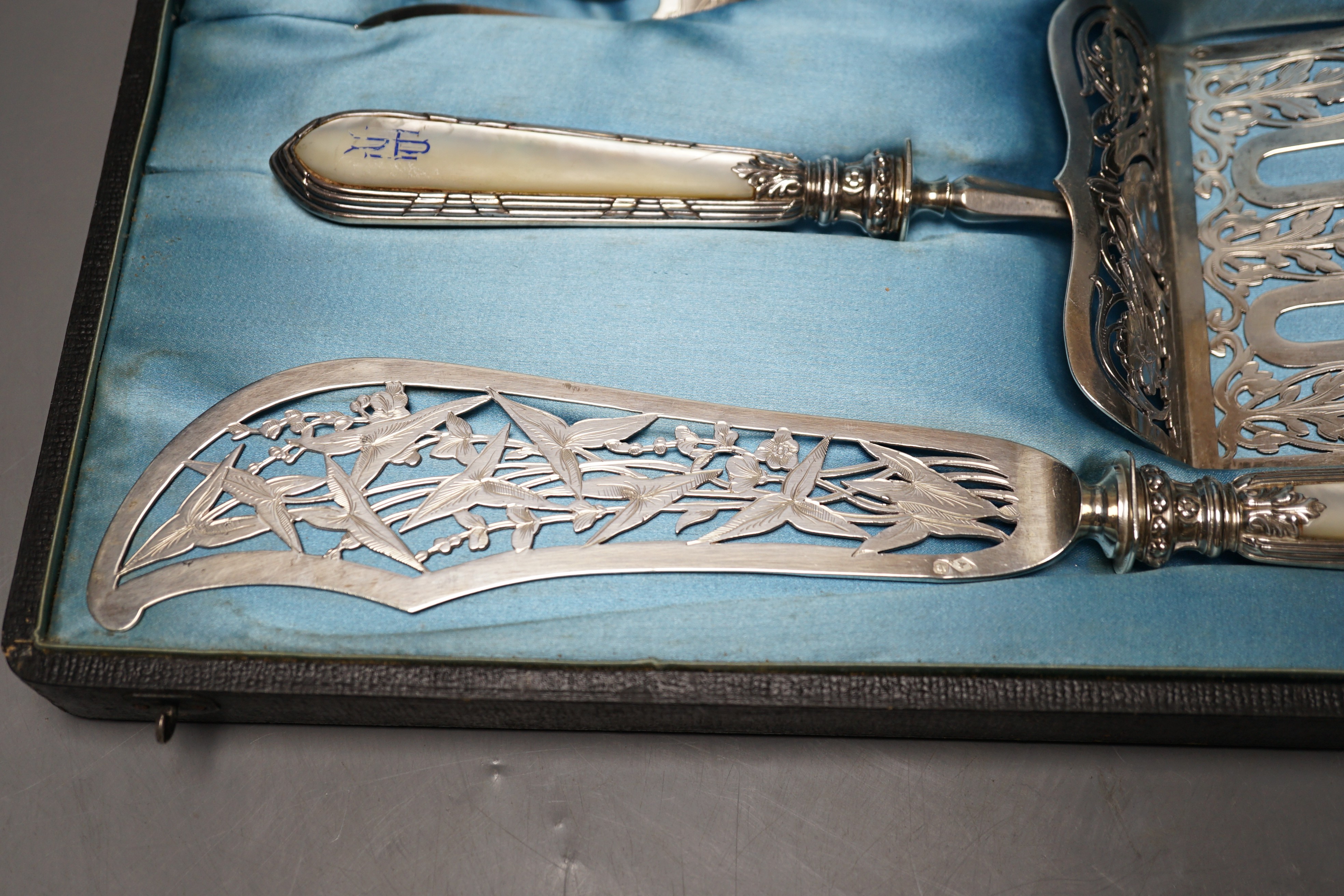 A cased ornate French white metal and mother of pearl mounted serving set, comprising a pair of fish servers and a cake server, maker JM.